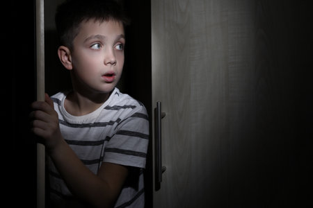 Scared little boy hiding in wardrobe. domestic violence conceptの写真素材