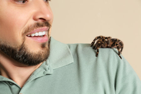 Scared man with tarantula on beige background, closeup. Arachnophobia (fear of spiders)