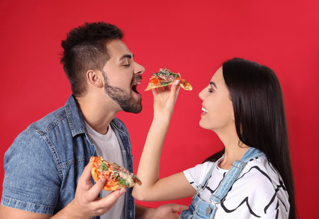 Happy young couple with pizza on red backgroundの写真素材