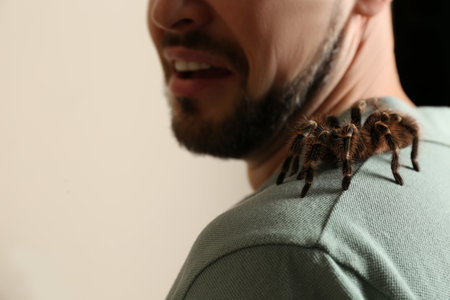 Scared man with tarantula on beige background, closeup. Arachnophobia (fear of spiders)の写真素材