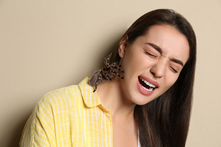Scared young woman with tarantula on beige background. Arachnophobia (fear of spiders)の写真素材