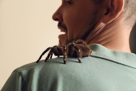 Scared man with tarantula on beige background, closeup. Arachnophobia (fear of spiders)の写真素材
