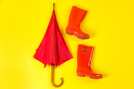 Beautiful red umbrella and rubber boots on light yellow background, flat layの写真素材