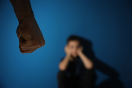 Man threatens his son on blue background, focus on hand. Domestic violence concept