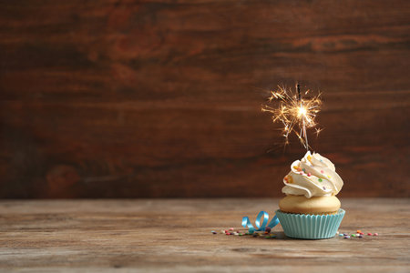 Birthday cupcake with sparkler on wooden table. Space for textの写真素材