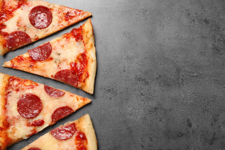 Slices of hot delicious pepperoni pizza on gray table, flat lay. Space for textの写真素材