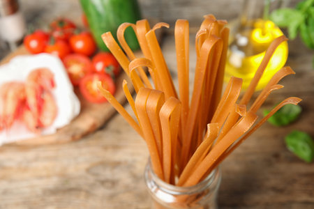 Jar with uncooked buckwheat noodles and fresh ingredients on wooden table, closeupの写真素材