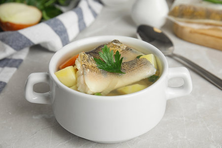 Delicious fish soup in bowl on light table, closeup