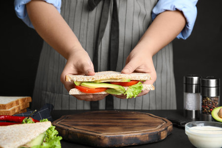 Woman holding tasty sandwich at black table, closeupの写真素材