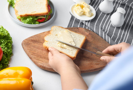 Woman spreading butter on sandwich at white table, closeupの写真素材