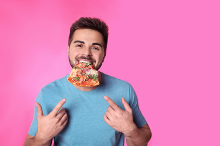 Handsome man eating pizza on pink backgroundの写真素材