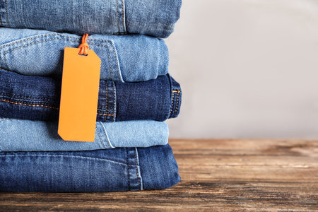 Stack of different jeans with tag on wooden table. Space for textの写真素材