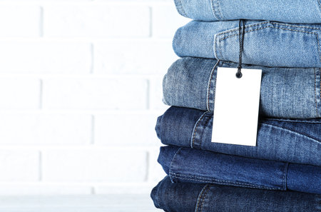 Stack of different jeans near white brick wall, closeup. Space for textの写真素材