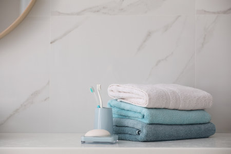 Stack of fresh towels, toothbrushes and soap bar on countertop in bathroom. Space for text