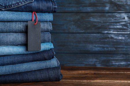 Stack of different jeans with tag on wooden table. Space for textの写真素材