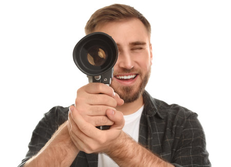 Young man with vintage video camera on white background, focus on lens