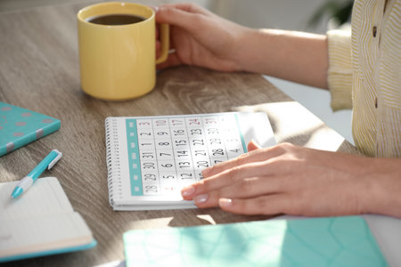 Woman with calendar and cup of drink at wooden table, closeupの写真素材