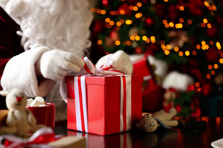 Santa Claus wrapping Christmas gift against blurred festive lights, closeupの写真素材