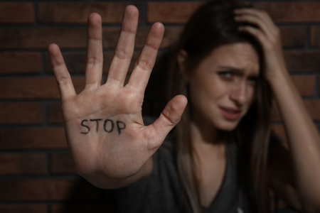 Abused young woman showing palm with word STOP near brick wall, focus on hand. domestic violence conceptの写真素材