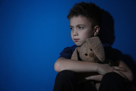 Sad little boy with toy near blue wall, space for text. domestic violence conceptの写真素材
