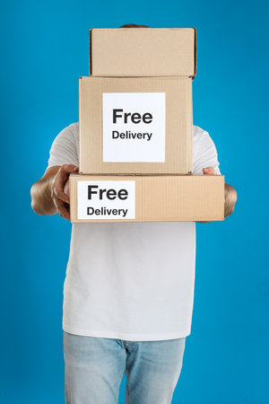 Male courier holding parcels with stickers Free Delivery on light blue backgroundの写真素材