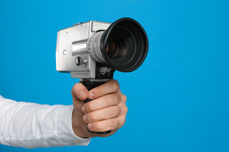 Man with vintage video camera on light blue background, closeup of hand