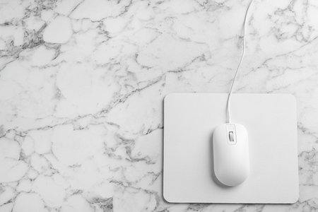 Modern wired optical mouse and pad on white marble table, top view. Space for textの写真素材