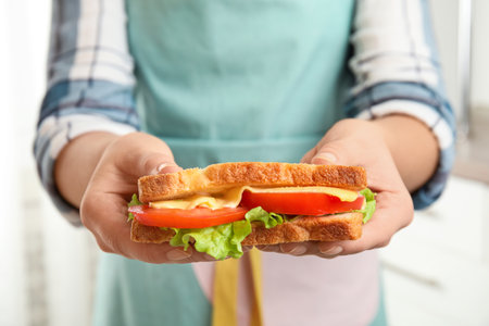 Woman holding tasty sandwich with cheese and tomato on light background, closeupの写真素材