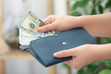 Woman putting money into wallet on blurred background, closeup