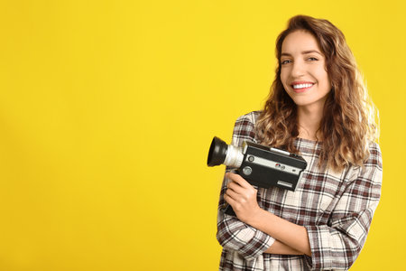 Beautiful young woman with vintage video camera on yellow background, space for textの写真素材