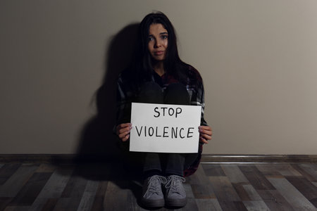 Abused young woman with sign STOP VIOLENCE near beige wallの写真素材