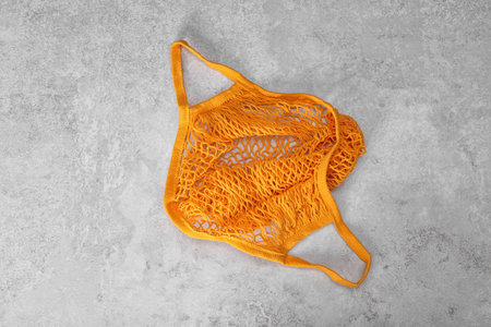 Orange net bag on light gray table, top view
