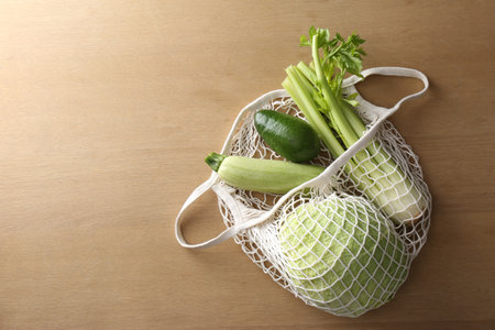 Different fresh vegetables in eco mesh bag on wooden table, top viewの写真素材