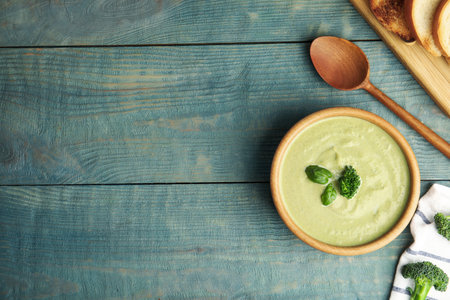 Delicious broccoli cream soup served on blue wooden table, flat lay. Space for textの写真素材