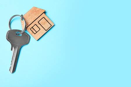 Key with trinket in shape of house on light blue background, top view and space for text. real...