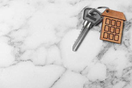 Key with trinket in shape of house on white marble background, top view and space for text. real estate agent servicesの写真素材