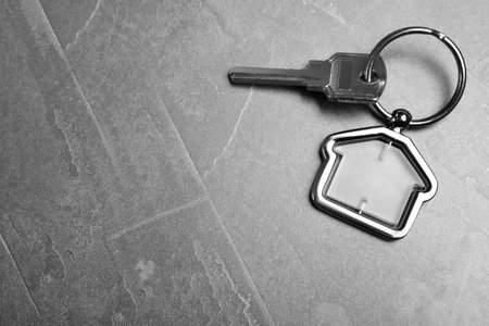 Key with trinket in shape of house on gray stone background, top view and space for text. real...