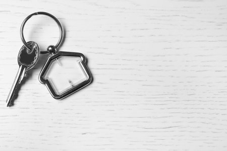 Key with trinket in shape of house on white wooden background, top view and space for text. real estate agent servicesの写真素材