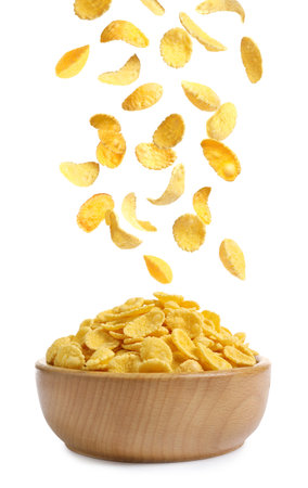 Tasty crispy corn flakes falling into bowl on white background