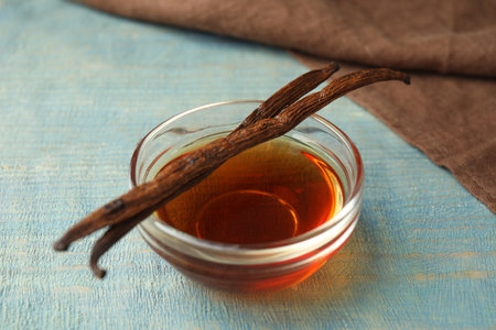Aromatic homemade vanilla extract on light blue wooden table, closeup
