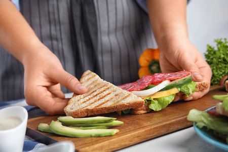 Woman making tasty sandwich with sausage at white table, closeupの写真素材