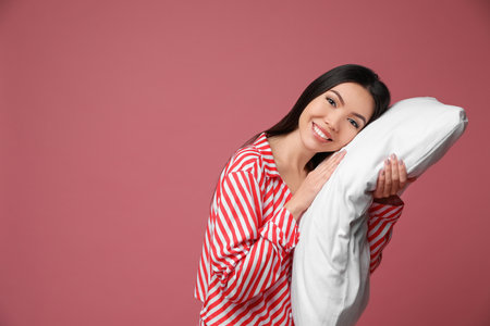 Beautiful Asian woman with pillow on dusty rose background, space for text. Bedtimeの写真素材