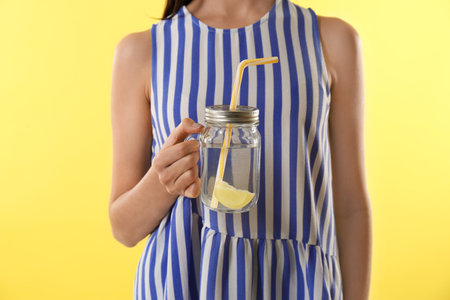 Young woman with tasty lemon water on yellow background, closeupの写真素材