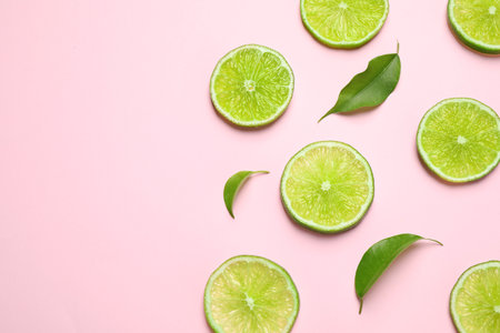 Juicy fresh lime slices and green leaves on pink background, flat lay. Space for textの写真素材