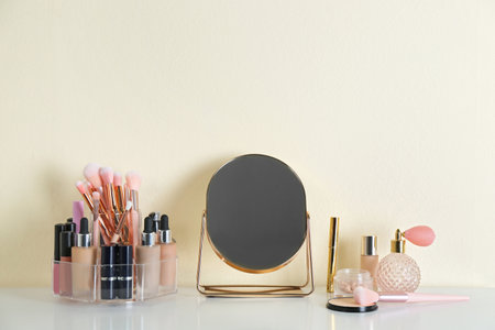 Mirror and makeup products on white table near light wallの写真素材