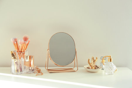 Small mirror and makeup products on white dressing table indoors