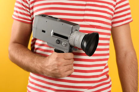 Man with vintage video camera on yellow background, closeupの写真素材