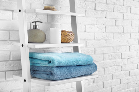 Clean soft towels and soap dispenser on shelves near white brick wallの写真素材
