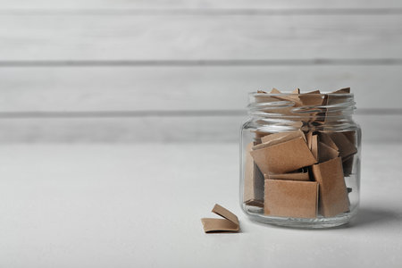 Glass jar with paper pieces on white table, space for textの写真素材