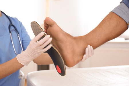 Female orthopedist fitting insole on patient's foot in clinic, closeupの写真素材